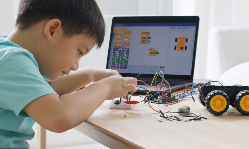 Young small kid happy smile self study online lesson excited make AI circuit toy. STEM STEAM digital scratch class on laptop screen for active children play arduino enjoy fun hobby.